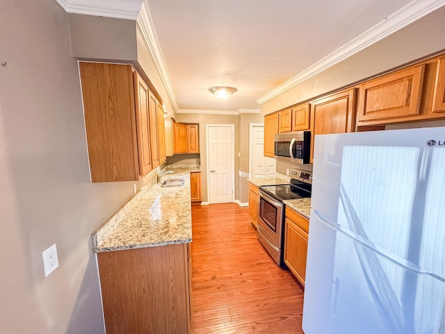 kitchen with appliances with stainless steel finishes, sink, light stone countertops, ornamental molding, and light hardwood / wood-style floors