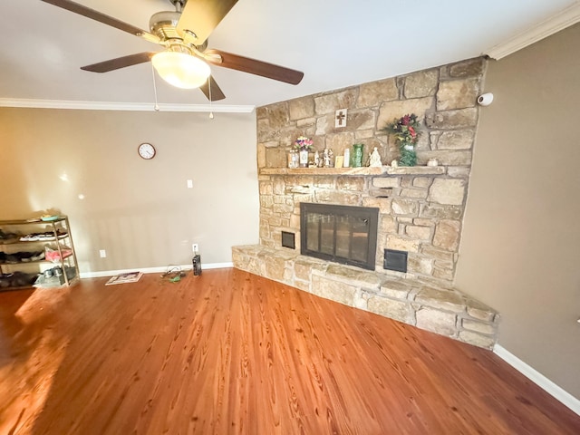 unfurnished living room with hardwood / wood-style flooring, a stone fireplace, ceiling fan, and ornamental molding