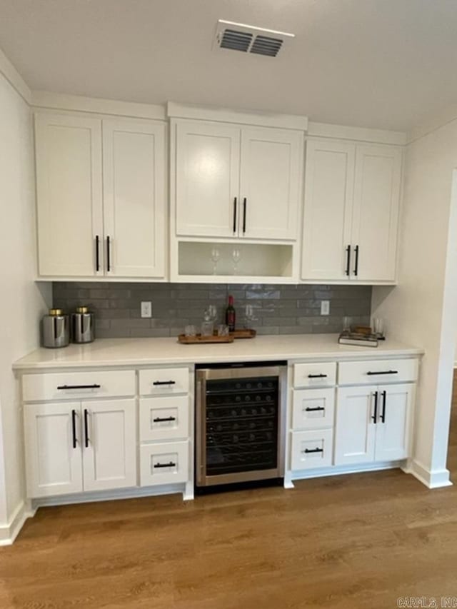 bar with tasteful backsplash, hardwood / wood-style floors, white cabinets, and beverage cooler