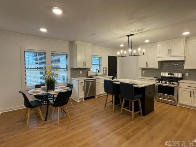 kitchen featuring pendant lighting, a center island, light wood-type flooring, appliances with stainless steel finishes, and white cabinetry