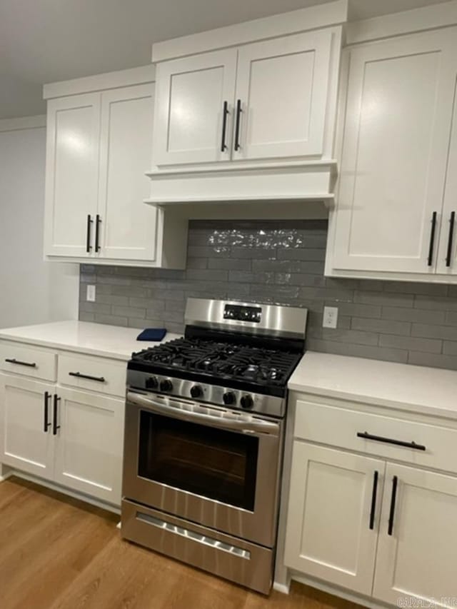 kitchen with stainless steel gas range oven, decorative backsplash, and white cabinets