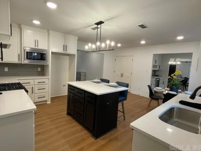 kitchen featuring stainless steel microwave, a kitchen island, a notable chandelier, decorative light fixtures, and white cabinets