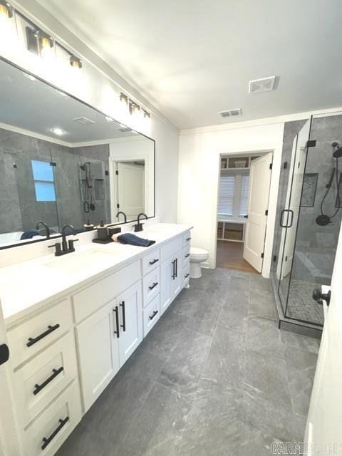 bathroom featuring vanity, toilet, a shower with door, and crown molding