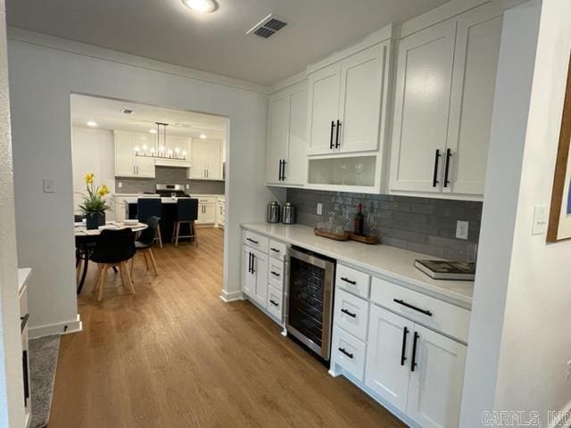 kitchen featuring hardwood / wood-style floors, backsplash, wine cooler, decorative light fixtures, and white cabinetry