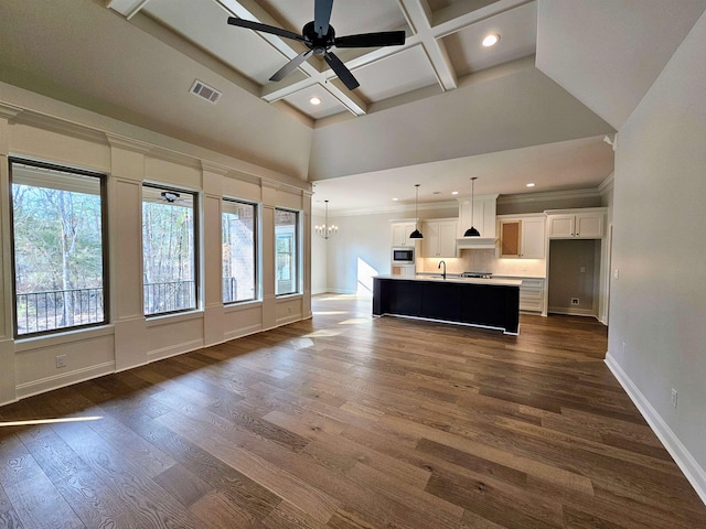 unfurnished living room with dark wood-type flooring, coffered ceiling, sink, beam ceiling, and ceiling fan with notable chandelier