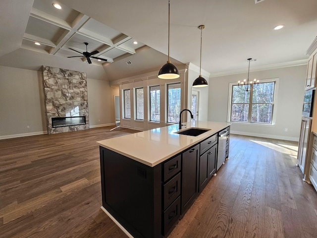 kitchen featuring a stone fireplace, dishwasher, sink, hanging light fixtures, and a kitchen island with sink