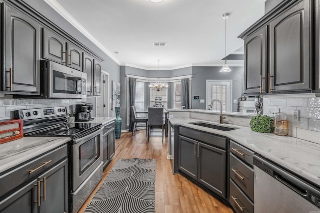 kitchen featuring pendant lighting, crown molding, sink, light stone counters, and stainless steel appliances