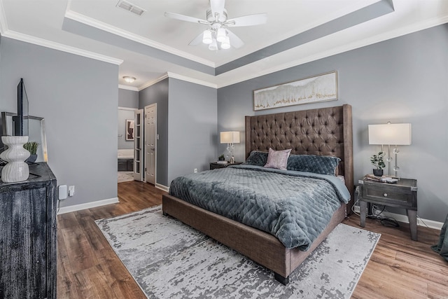 bedroom featuring ensuite bath, ceiling fan, crown molding, a tray ceiling, and hardwood / wood-style flooring