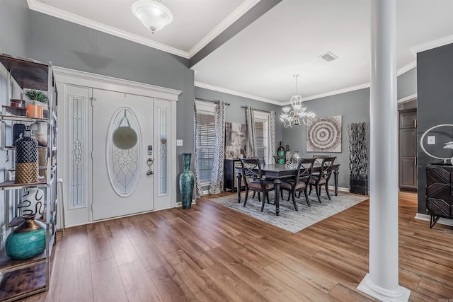 foyer with hardwood / wood-style flooring, an inviting chandelier, crown molding, and decorative columns