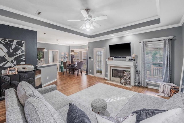 living room featuring ceiling fan with notable chandelier, light wood-type flooring, crown molding, and a tray ceiling