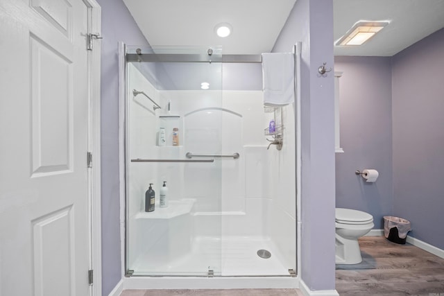 bathroom with toilet, a shower with shower door, and wood-type flooring