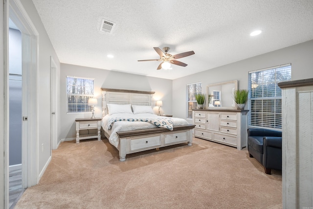 bedroom featuring a textured ceiling, ceiling fan, light carpet, and multiple windows