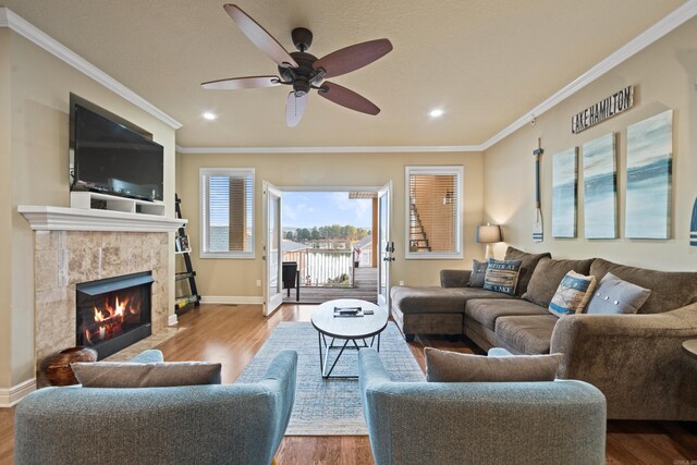 living room featuring wood-type flooring, ceiling fan, ornamental molding, and a tiled fireplace