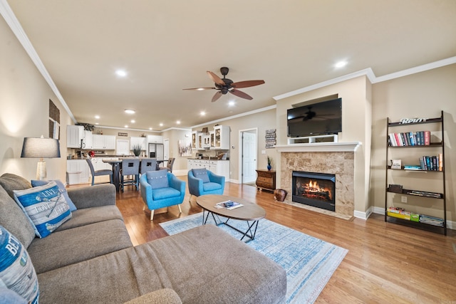 living room featuring ceiling fan, light hardwood / wood-style floors, a premium fireplace, and crown molding