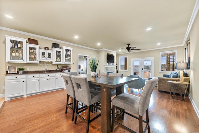 dining space featuring french doors, light wood-type flooring, ornamental molding, ceiling fan, and indoor bar