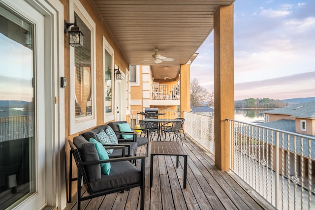 balcony at dusk with outdoor lounge area, a water view, and ceiling fan