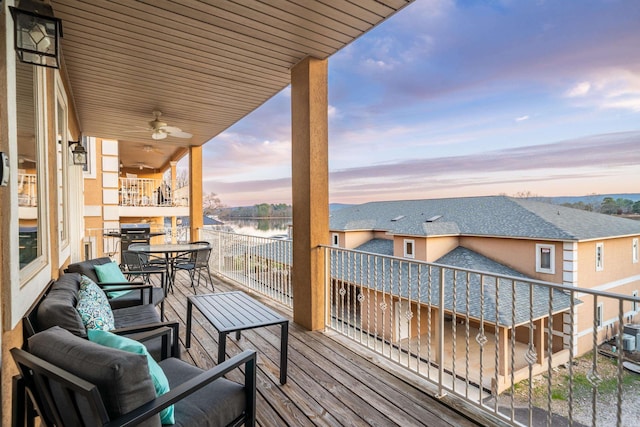 balcony at dusk featuring an outdoor living space, ceiling fan, and a water view