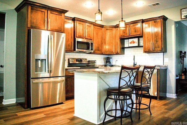 kitchen with pendant lighting, light stone countertops, a kitchen island, a kitchen bar, and stainless steel appliances