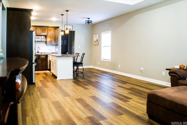 kitchen featuring backsplash, decorative light fixtures, hardwood / wood-style flooring, a center island, and a breakfast bar area