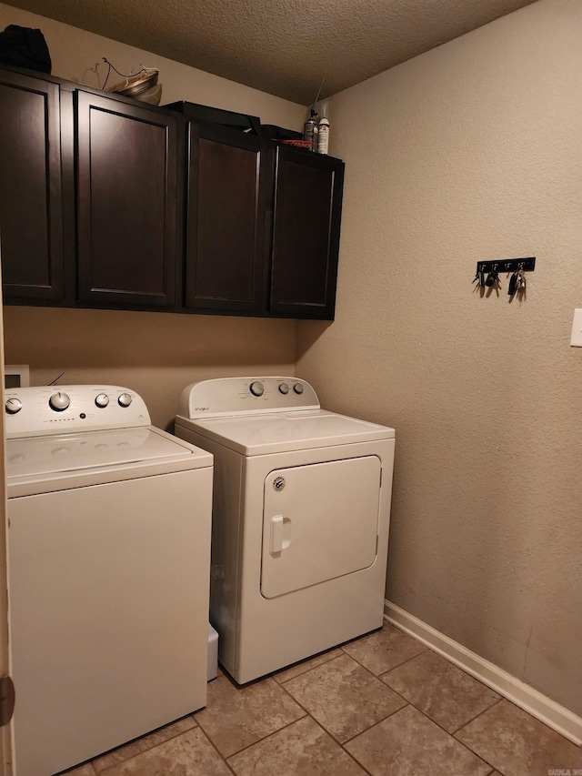 clothes washing area featuring washing machine and clothes dryer, cabinets, and a textured ceiling