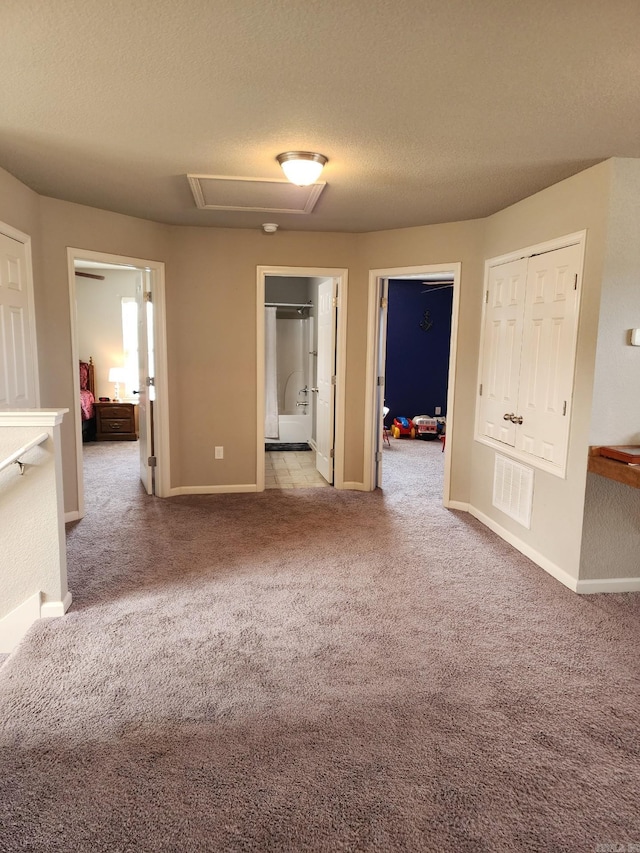 unfurnished bedroom featuring a textured ceiling, light colored carpet, ensuite bath, and a closet