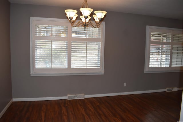 spare room featuring a healthy amount of sunlight, dark wood-type flooring, and an inviting chandelier