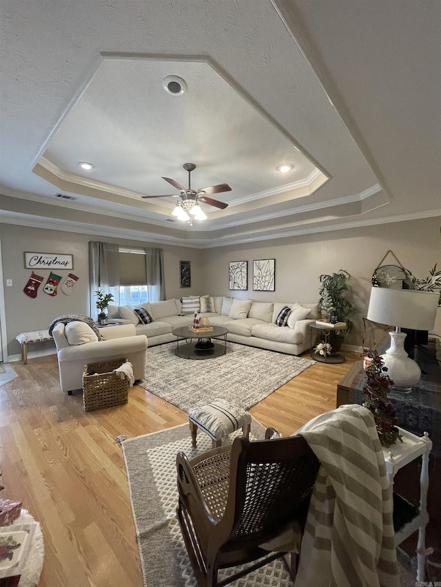 living room with hardwood / wood-style flooring, a raised ceiling, and ornamental molding