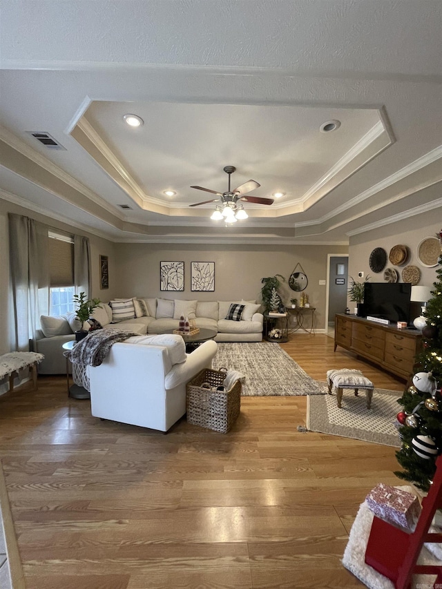 living room with ceiling fan, wood-type flooring, crown molding, and a tray ceiling