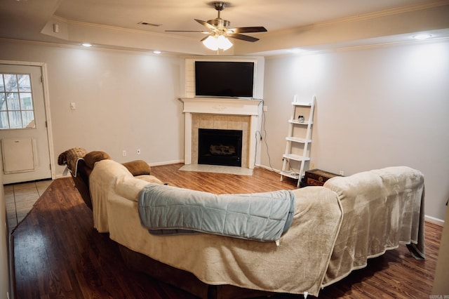 living room featuring a tray ceiling, ceiling fan, crown molding, a tile fireplace, and hardwood / wood-style floors