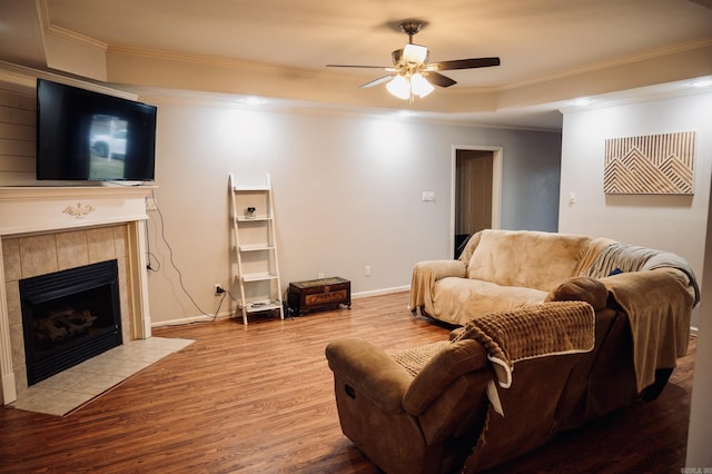 living room with ceiling fan, wood-type flooring, ornamental molding, and a tile fireplace