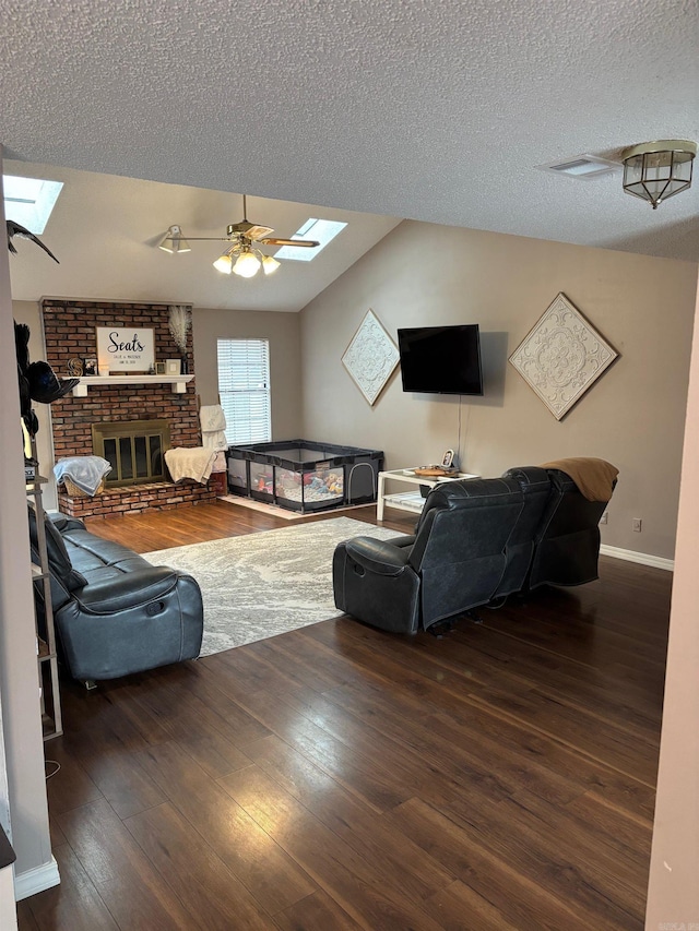 living room featuring a skylight, ceiling fan, dark hardwood / wood-style floors, and a brick fireplace