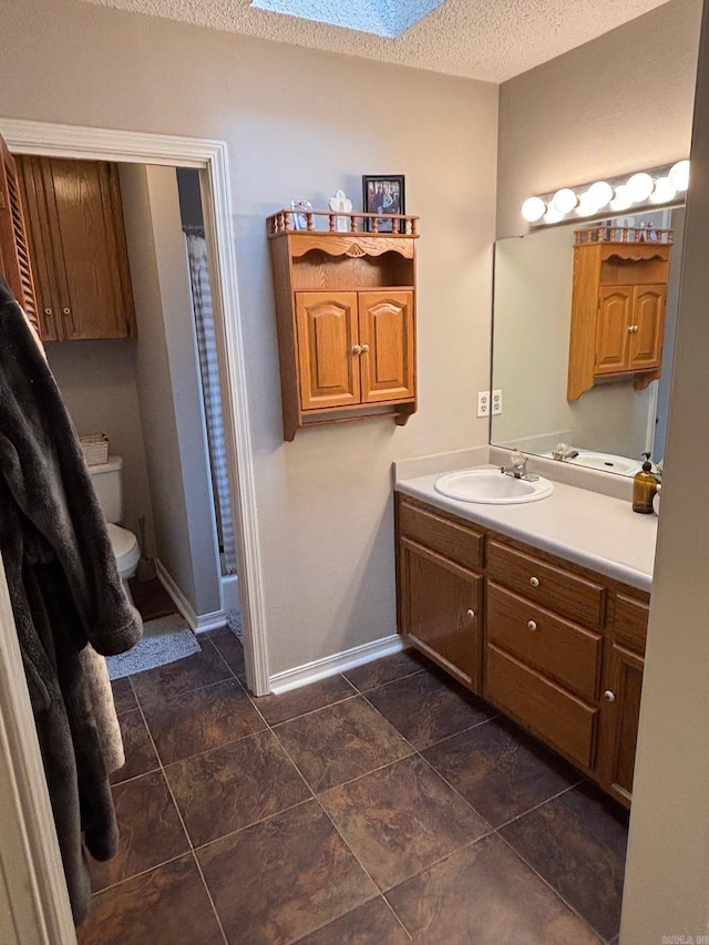 bathroom featuring a shower with shower curtain, a skylight, vanity, a textured ceiling, and toilet