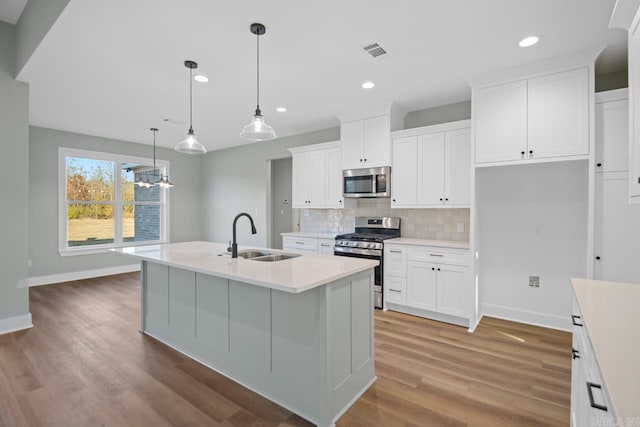 kitchen with a center island with sink, sink, appliances with stainless steel finishes, decorative light fixtures, and white cabinetry