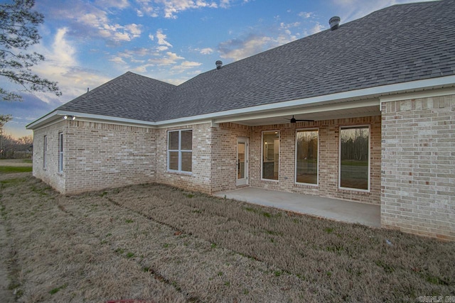 back house at dusk with ceiling fan, a patio area, and a lawn