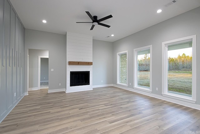 unfurnished living room with ceiling fan, a large fireplace, and light hardwood / wood-style flooring