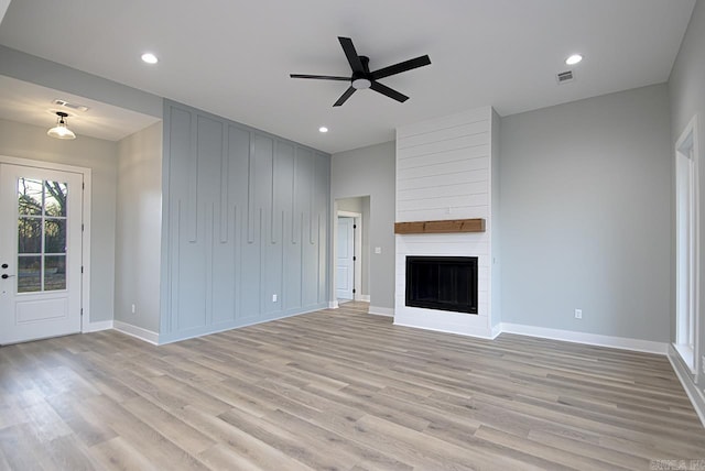 unfurnished living room with ceiling fan, a large fireplace, and light hardwood / wood-style floors