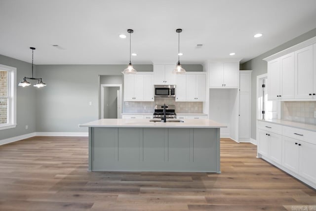 kitchen with white cabinets, hanging light fixtures, a kitchen island with sink, and appliances with stainless steel finishes