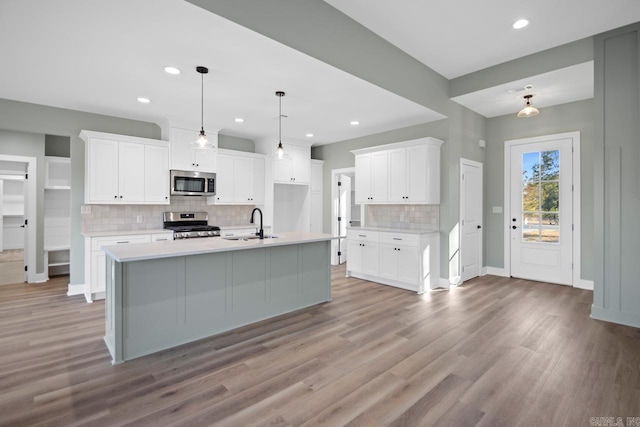 kitchen with white cabinets, decorative light fixtures, an island with sink, and appliances with stainless steel finishes