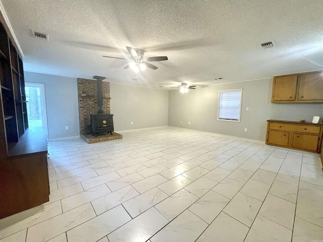 unfurnished living room with a textured ceiling, a wood stove, plenty of natural light, and ceiling fan