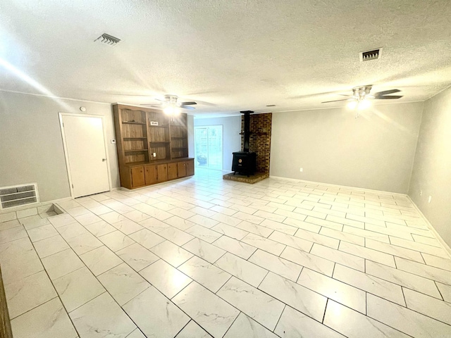 unfurnished living room with ceiling fan, a wood stove, and a textured ceiling