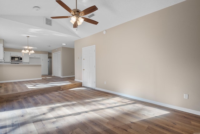 unfurnished living room with ceiling fan with notable chandelier, light hardwood / wood-style floors, and vaulted ceiling