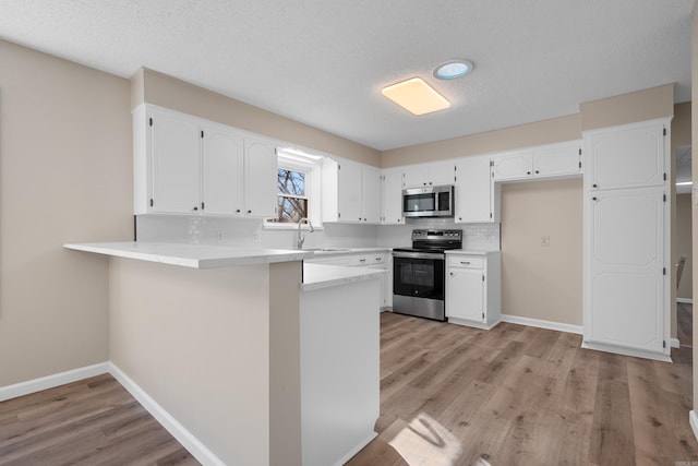 kitchen featuring kitchen peninsula, sink, light hardwood / wood-style flooring, appliances with stainless steel finishes, and white cabinetry