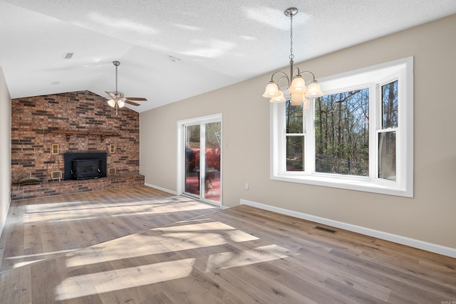 unfurnished living room featuring ceiling fan with notable chandelier, a textured ceiling, hardwood / wood-style floors, a wood stove, and lofted ceiling