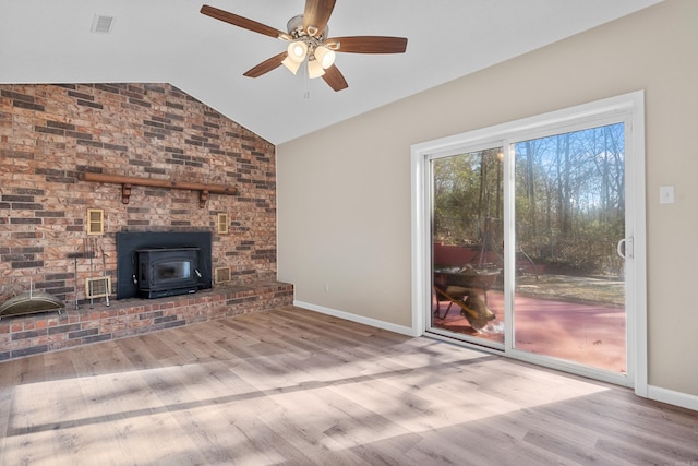 unfurnished living room featuring ceiling fan, a wood stove, light hardwood / wood-style flooring, and vaulted ceiling