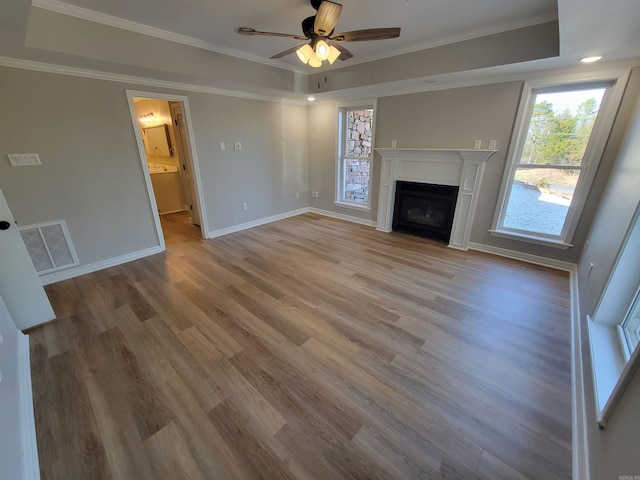 unfurnished living room featuring ceiling fan, wood-type flooring, ornamental molding, and a tray ceiling