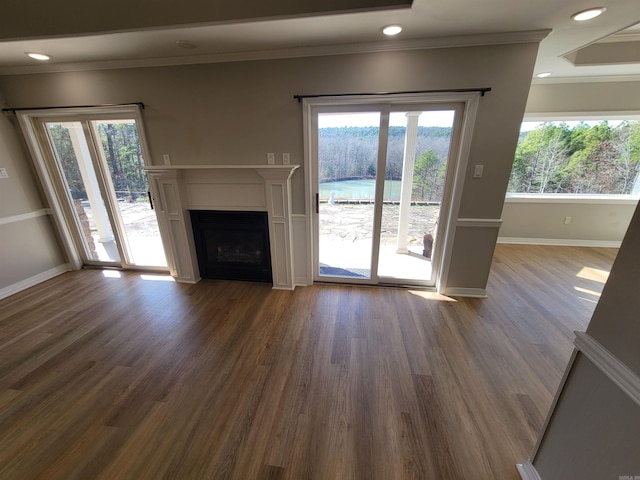 unfurnished living room with wood-type flooring, a wealth of natural light, and ornamental molding