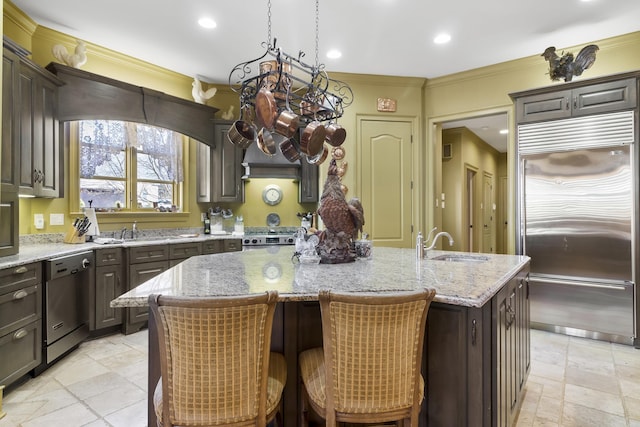 kitchen with dark brown cabinetry, light stone countertops, sink, stainless steel appliances, and a center island with sink