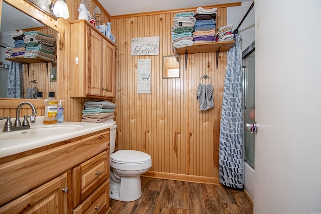 full bathroom with bath / shower combo with glass door, toilet, wooden walls, vanity, and hardwood / wood-style flooring