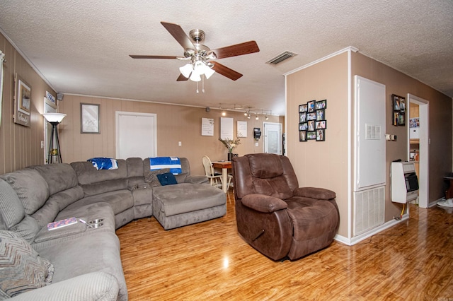 living room featuring a textured ceiling, light wood-type flooring, ceiling fan, and wood walls