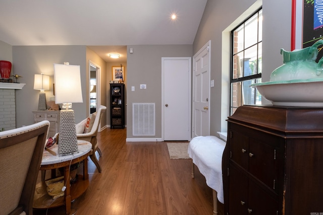 living area with a brick fireplace, light hardwood / wood-style floors, and vaulted ceiling